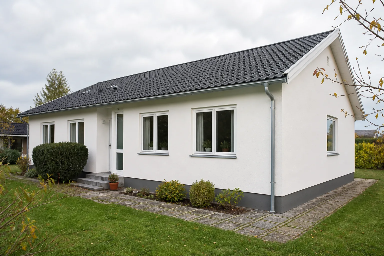 Dansk parcelhus med lys pudset facade, mørk sokkel og hvide vinduer